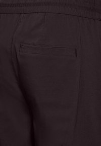Dunkle Stoffhosen mit einem elastischen Bund, versehen mit einer einzelnen hinteren Tasche. Glatte Textur und minimalistisches Design.