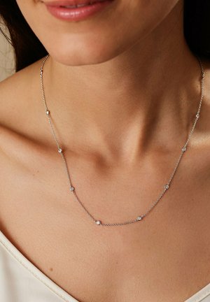 Zilveren ketting met kleine ronde accenten met heldere stenen, gedragen rond de nek op een gladde, naakte huid.