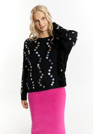 Pulover negru cu embellishementi colorati din paiete, asortat cu o fustă tricotată roz. Puloverul are o croială lejeră și texturi distinctive.