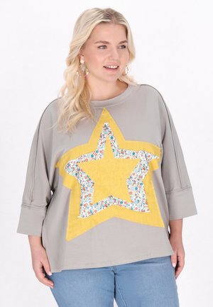 Grå oversized t-shirt med en stor gul stjerne med blomstermønster i midten. Stoffet ser blødt ud, med trekvartærmer.
