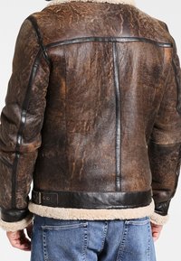 Blouson en cuir marron avec col en peau lainée, présentant une apparence texturée et usée, des accents en cuir noir, et une ceinture à la taille.