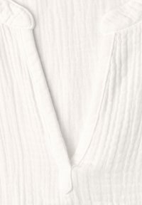 Gros plan d'un tissu blanc texturé avec un col en V et un motif quadrillé subtil sur un matériau doux.