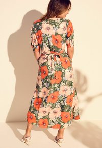 Blumenkleid in Midi-Länge in Grün, mit großen orangefarbenen und pinken Blumen, kurzen Ärmeln und einem Bindegürtel in der Taille. Glattes, leichtes Material.