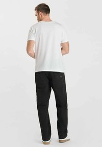 Witte T-shirt met korte mouwen in combinatie met zwarte broek, met een ontspannen pasvorm en een soepele textuur. Witte sneakers maken de outfit compleet.