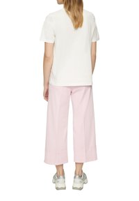 T-shirt en coton blanc associé à un pantalon à jambes larges rose clair, avec une coupe droite et un ourlet large. Complété par des baskets grises et blanches.