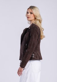 Giacca da moto in suede marrone con cerniere e lacci laterali. Presenta una vestibilità aderente, una consistenza morbida e una chiusura a bottone a pressione sul colletto.