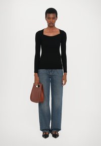 Svart ribbestrikket langermet topp med firkantet hals, kombinert med lyseblå vide jeans. Modellen holder en brun skinnveske og har på seg svarte sko.