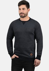 Donkergrijze sweatshirt met een ronde hals, raglanmouwen en een driehoekige accent aan de borst. Bevat een leren merklabel aan de zoom.