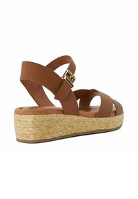 Brown leather wedge sandal with crisscross straps, gold buckle, and woven straw platform sole.