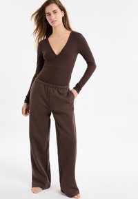 Brązowe, prążkowane body z długim rękawem i głębokim dekoltem w serek, zestawione z luźnymi brązowymi spodniami z elastycznym pasem.