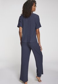 Temno modri komplet udobne obleke, ki vključuje kratkosleeven zgornji del ohlapnega kroja z rebrastim teksturo in široke hlače, oboje izdelano iz mehkega materiala.