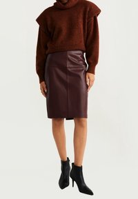 Ruskea neulottu pooloneule, löysä istuvuus, lyhyet hihat, yhdistetty korkeavyötäröiseen viininpunaiseen nahkaiseen kynähameeseen. Mustat nilkkurit.