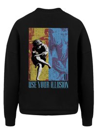 Schwarzer Pullover mit einem grafischen Design auf der Rückseite, das gelbe und blaue Abschnitte zeigt, eine Figur in Bewegung darstellt und den Text "NUTZE DEINE Illusion" enthält.