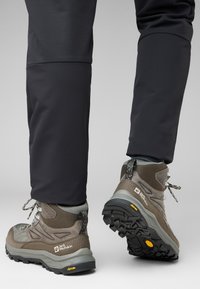 Scarpe da trekking marroni realizzate in pelle e rete, con suola robusta e un battistrada prominente, accenti grigi e lacci riflettenti.