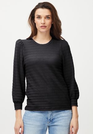 Cămașă lungă cu mâneci negre, texturată, cu model în dungi, croi lejer, decolteu rotund și detalii plisate la umeri, purtată cu blugi de color albastru deschis.