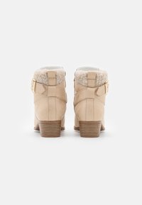 Beige kotníkové boty s semišovým povrchem, límcem z umělé kožešiny, postranními přezkami a vrstveným podpatkem s vodorovnými drážkami.