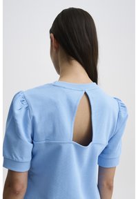 Felpa azzurra chiaro con maniche puff corte, caratterizzata da un'apertura a chiave sul retro e una superficie liscia.
