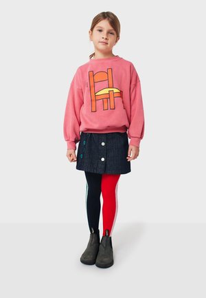 Pink sweatshirt with graphic design, navy corduroy skirt, multicolored leggings, and black ankle boots. Notable button accents on skirt.
