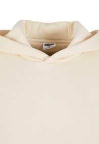 Sweat à capuche couleur crème avec capuche repliée et étiquette "Urban Class" visible à l'intérieur du col, taille M.