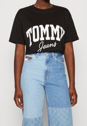 Černé zkrácené tričko s výrazným bílým potiskem "TOMMY Jeans", spárované s džínami s vysokým pasem ve světle modré barvě s patchworkovým vzorem a texturovanými akcenty.
