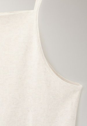 Gros plan d’un haut en tissu blanc sans manches montrant les détails des coutures au niveau de l’encolure et de la couture d’épaule sur un fond uni.