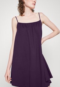 Vestido roxo sem mangas, feito de tecido suave, com um decote franzido e silhueta ampla, apresentando alças finas e uma textura lisa.