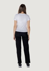 Witte T-shirt met korte mouwen en een gladde textuur, gecombineerd met zwarte broek en sportschoenen, die een casual outfit vanuit een achteraanzicht laat zien.