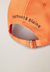 Oranžová čiapka s vyšitým textom "harmont & blaine" v námorníckej farbe. Obsahuje textilný popruh a kovové nastavovacie príslušenstvo. Hladká štruktúra.