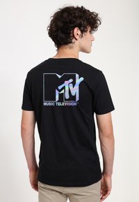 Sort bomulds t-shirt med et holografisk MTV-logo og teksten "MUSIC TELEVISION" på ryggen. Korte ærmer og klassisk crew neck design.