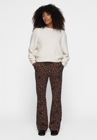 Suéter de color beige claro con un corte holgado y puños acanalados, combinado con pantalones marrones de campana que presentan un estampado de leopardo negro.
