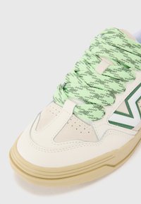 Fehér sneaker sima bőr és velúr felsőrésszel, zöld chevron logóval, texturált menta zöld fűzőkkel és világos barna gumitalppal.