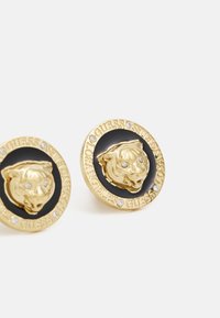 Gold-tone earrings featuring a raised tiger head on a black circular backdrop. Accented with clear rhinestones and embossed text.