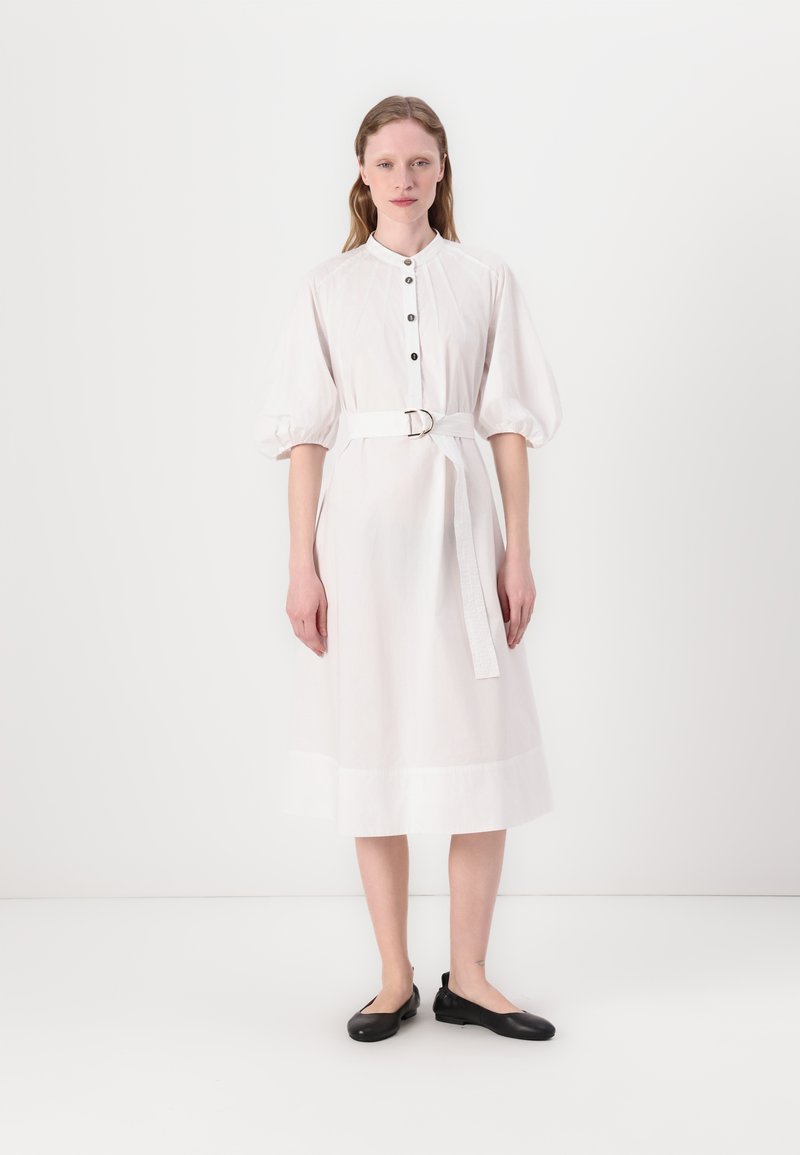 Hvit midi-kjole med krage, knappestolpe foran og korte pufferm; innsnevret midje med stoffbelte, glatt tekstur og minimalistisk design.