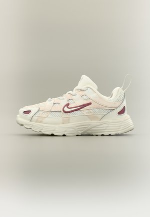 Weißer und beiger Nike-Sneaker mit dunkelrotem Swoosh-Logo, Mesh-Einsätzen, gepolstertem Kragen und strukturierter Sohle, seitlich dargestellt vor neutralem Hintergrund.