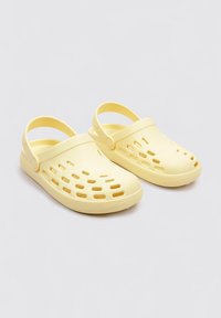 Sabots en plastique jaune avec des trous de ventilation découpés, un bout rond et une sangle arrière pour un maintien sécurisé. Texture lisse et design léger.