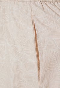 Tissu beige clair avec un motif linéaire blanc abstrait. Présente une coupe décontractée et une taille élastique avec des détails de texture et de couture subtils.
