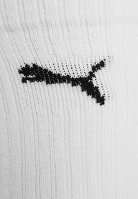 Logo de Puma negro tejido en la tela de un textil blanco acanalado, probablemente un calcetín o una manga.