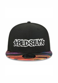 Black snapback cap with "BED.STUY" embroidered in white. Colorful patterned visor features vibrant stripes in orange, pink, and blue.