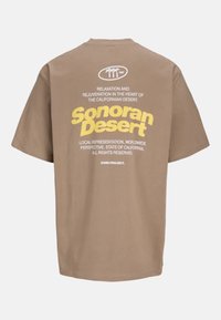 Bruine katoenen T-shirt met korte mouwen en een ronde hals. Bevat witte en gele tekst op de achterkant, waaronder "Sonoran Desert" en grafische accenten.