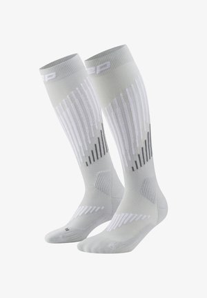 Een paar witte kniehoge compressiesokken met grijs en witte verticale strepen en geribbelde enkelsupport.