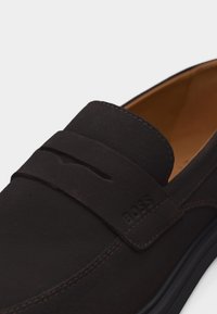 Mocassin à enfiler en cuir marron foncé avec détail de bride et logo "BOSS" embossé, doté d'une doublure intérieure beige et d'une semelle noire.