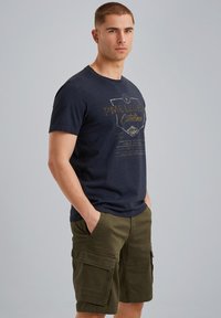 Navy blue short-sleeve t-shirt with a printed design on the front, paired with olive green cargo shorts featuring multiple zippered pockets.