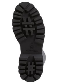 Suela de bota de goma negra con profundas protuberancias de tracción, que presenta un patrón de hashtag y un logo circular. Diseño funcional para estabilidad y agarre.
