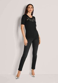 Schwarzes kurzärmeliges Oberteil mit strukturierten Details, kombiniert mit engen schwarzen Jeans und silbernen spitzen Absätzen, die eine elegante Silhouette und klare Linien aufweisen.