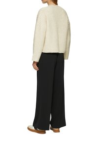 Chunky crèmekleurige trui met een boxy fit, geribbelde textuur en brede mouwen, gecombineerd met losse zwarte broeken en beige schoenen.