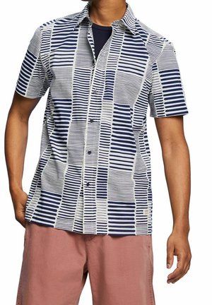 Kortærmet skjorte med knapper i hvid med navy blå stribemønster. Har en klassisk krave og frontknapper, parret med lyserøde shorts.