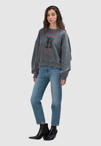 Szara, oversize bluza z nadrukiem, zestawiona z jasnoniebieskimi dżinsami i czarnymi botkami za kostkę. Posiada luźny krój i prążkowane mankiety.