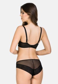 Černá souprava spodního prádla obsahující průhlednou podprsenku se zvlněnými okraji a odpovídajícími kalhotkami typu boyshorts. Materiál je hladký s průsvitným designem.