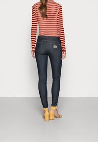 Donkere blauw skinny jeans van denim, met een hoge taille, achterzakken en oranje stiksel. Gecombineerd met een rood-wit gestreept topje.