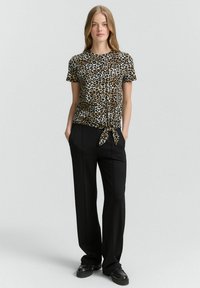 Majica kratkih rukava sa leopard printom, izrađena od lagane tkanine, s povezanom dekoracijom na struku, u kombinaciji s hlačama viskog struka u crnoj boji.